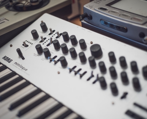 A white korg minilogue synthesizer with many knobs.