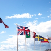 Several national flags flying against a cloudy sky.
