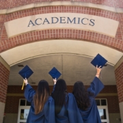 three girls in graduation gowns hold their caps in the air