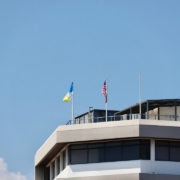 Two flags fly on a modern building rooftop.