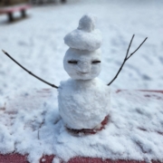 A small snowman sitting on top of snow covered ground