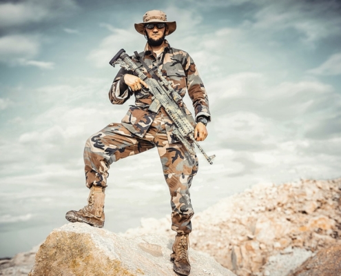 man wearing brown and green camouflage uniform holding rifle while standing on rock