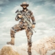 man wearing brown and green camouflage uniform holding rifle while standing on rock