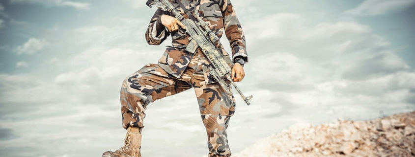 man wearing brown and green camouflage uniform holding rifle while standing on rock