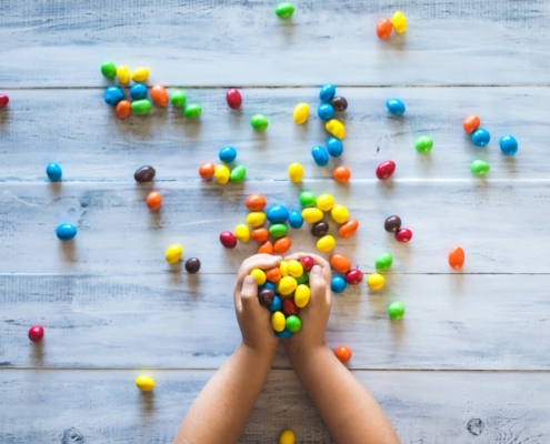 selective photo of kid holding candies on gray wooden pallet board