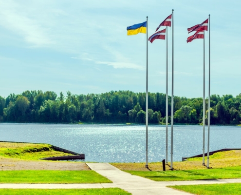 Three flags fly near a tranquil lake and forest.