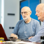 two men sitting at a table looking at a laptop