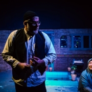 Two people on a dimly lit stage set.