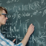Young man writing mathematical formulas on a chalkboard.