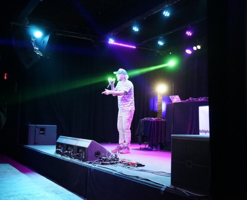 A man speaking on a stage with colorful lights.