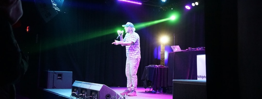 A man speaking on a stage with colorful lights.
