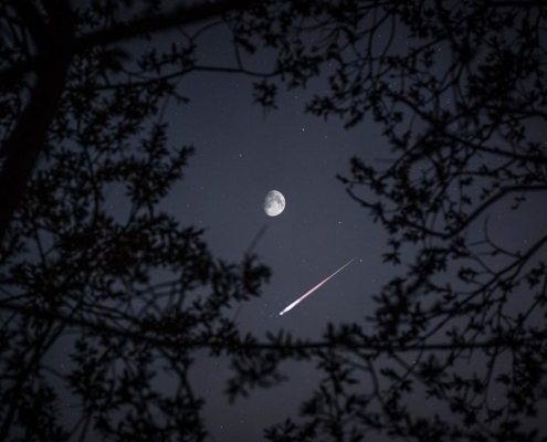 A meteor streak under the moon and stars.