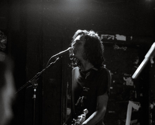 greyscale photo of man singing while holding guitar