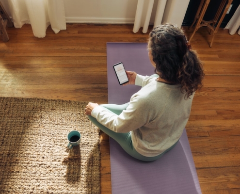 Woman meditating on yoga mat with phone and drink.