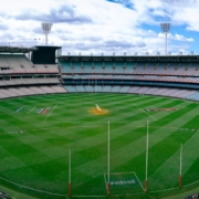 a sports stadium with a field and a field with a crowd of people with Melbourne Cricket Ground in the background