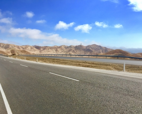 gray concrete road near brown mountain under blue sky during daytime