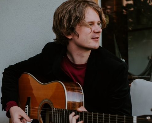 man in black long sleeve shirt playing brown acoustic guitar