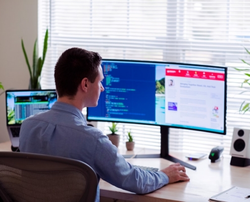 man in gray dress shirt sitting on chair in front of computer monitor
