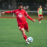 man in red soccer jersey kicking soccer ball on green grass field during daytime
