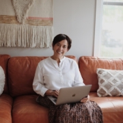 man in white dress shirt sitting on red couch using silver macbook
