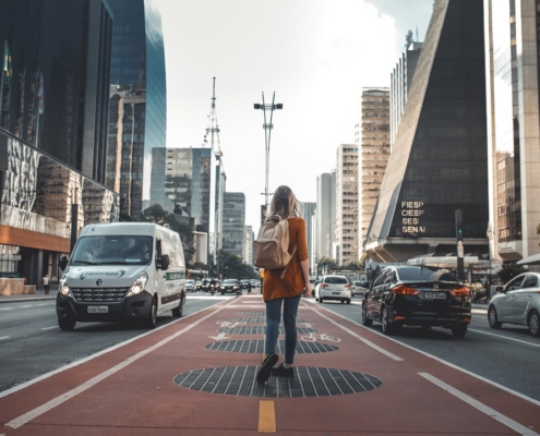 photography of woman walking in between road with vehicles