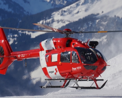 red and white helicopter flying over snow covered mountain during daytime