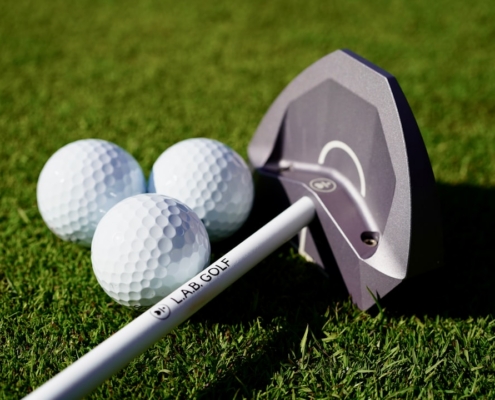 Three golf balls and a putter on green grass.