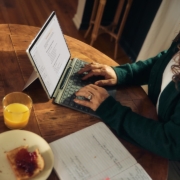 Woman typing on laptop at wooden table with breakfast.