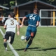 2 men playing soccer on green grass field during daytime
