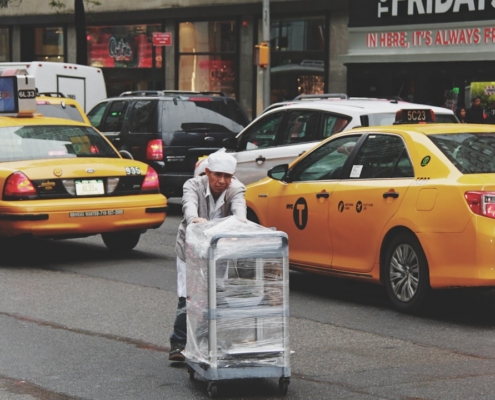 man pushing gray bus cart on road near two yellow taxi cabs