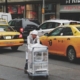 man pushing gray bus cart on road near two yellow taxi cabs