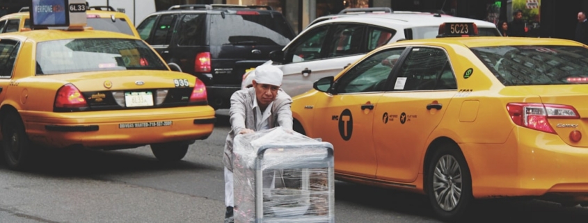 man pushing gray bus cart on road near two yellow taxi cabs