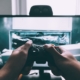 person holding game controller in-front of television