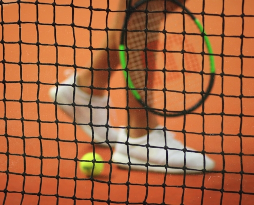 person wearing pair of white low-top sneakers while holding Wilson tennis racket