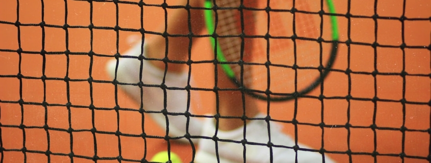 person wearing pair of white low-top sneakers while holding Wilson tennis racket