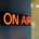 Red neon "on air" sign glowing on wall.
