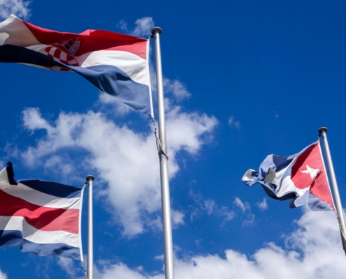 Three national flags waving against a blue sky