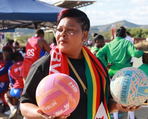 Woman holds two netballs at a netball game.